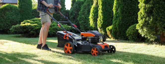 Photo of Man cutting green grass with lawn mower in garden
