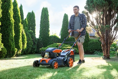 Photo of Man cutting green grass with lawn mower in garden