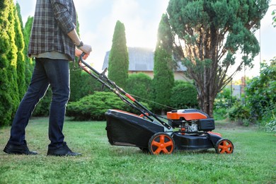 Photo of Man cutting green grass with lawn mower in garden, closeup