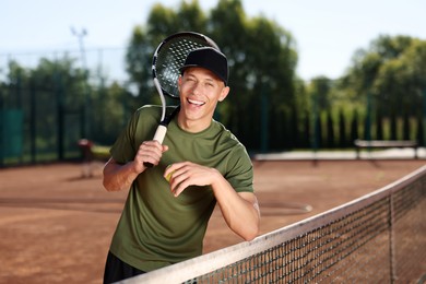 Photo of Smiling young man with racket and ball at tennis court
