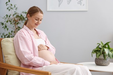 Photo of Beautiful pregnant woman in armchair at home. Space for text