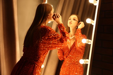 Photo of Beautiful woman applying mascara while getting ready near mirror indoors