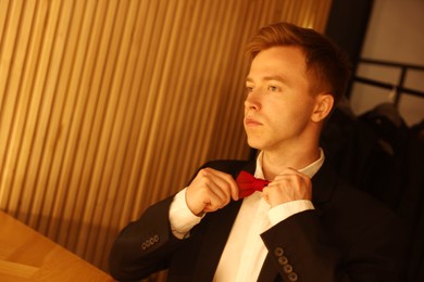 Photo of Man adjusting bow tie while getting ready at dressing table indoors