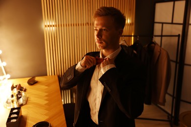 Photo of Man adjusting bow tie while getting ready at dressing table indoors