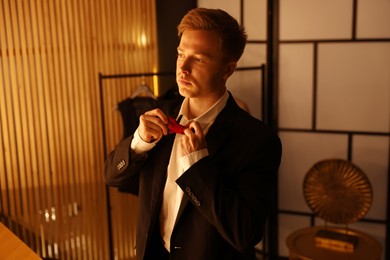 Photo of Man adjusting bow tie while getting ready indoors