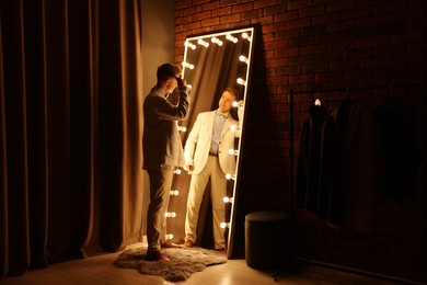 Photo of Handsome man brushing his hair while getting ready near mirror indoors