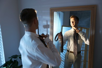 Photo of Man choosing neckties while getting ready near mirror indoors