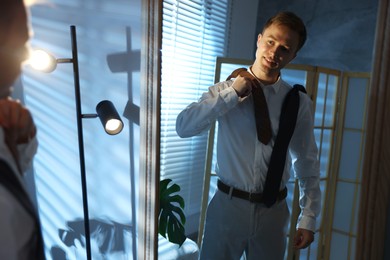 Photo of Man choosing neckties while getting ready near mirror indoors