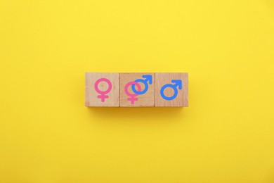 Image of Sex education. Wooden cubes with female and male gender symbols on yellow background, top view