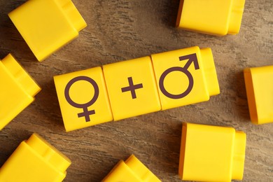 Image of Sex education. Yellow cubes with female and male gender symbols and plus sign on wooden background, top view