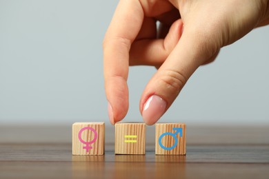 Image of Sex education. Woman putting cube with equals sign between cubes with female and male gender symbols on wooden table, closeup