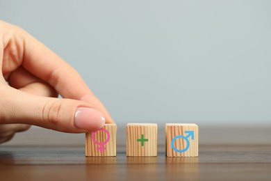 Image of Sex education. Woman putting cube with female gender symbol next to cubes with plus sign and male symbol on table, closeup