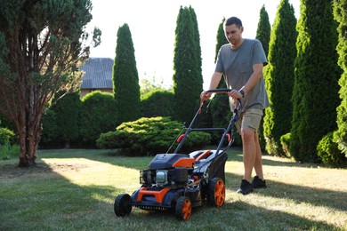 Photo of Man cutting green grass with lawn mower in garden
