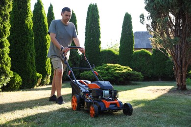 Photo of Man cutting green grass with lawn mower in garden