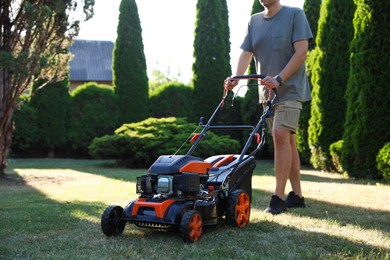 Photo of Man cutting green grass with lawn mower in garden, closeup