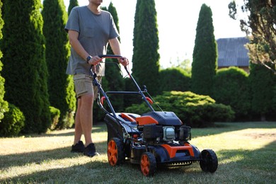 Photo of Man cutting green grass with lawn mower in garden, closeup