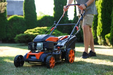 Photo of Man cutting green grass with lawn mower in garden, closeup