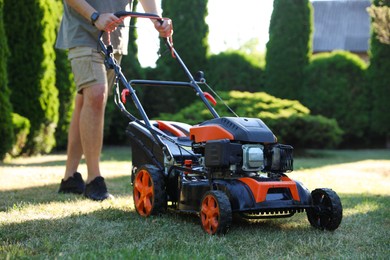 Photo of Man cutting green grass with lawn mower in garden, closeup