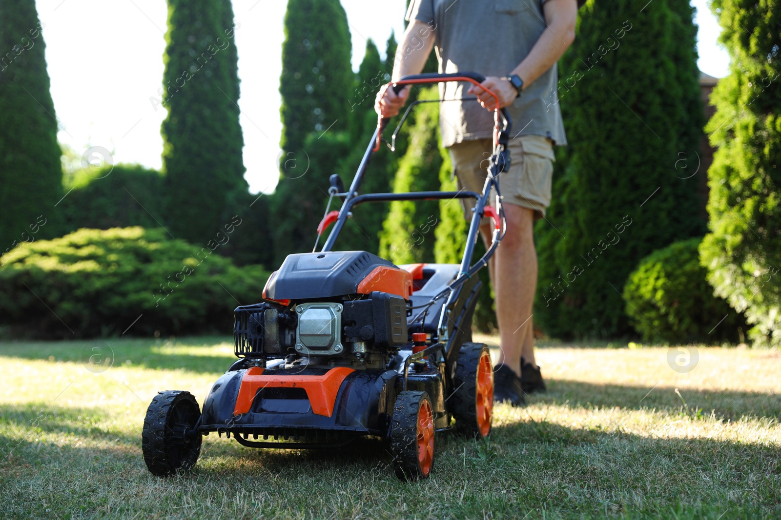 Photo of Man cutting green grass with lawn mower in garden, closeup
