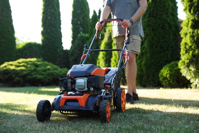 Photo of Man cutting green grass with lawn mower in garden, closeup