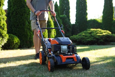 Photo of Man cutting green grass with lawn mower in garden, closeup