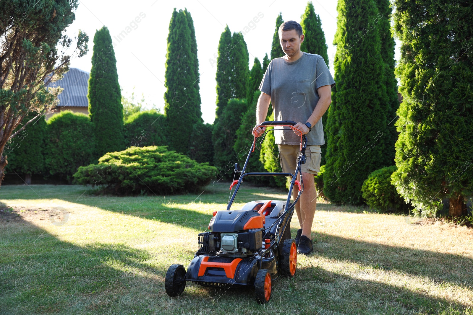 Photo of Man cutting green grass with lawn mower in garden
