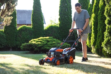 Photo of Man cutting green grass with lawn mower in garden