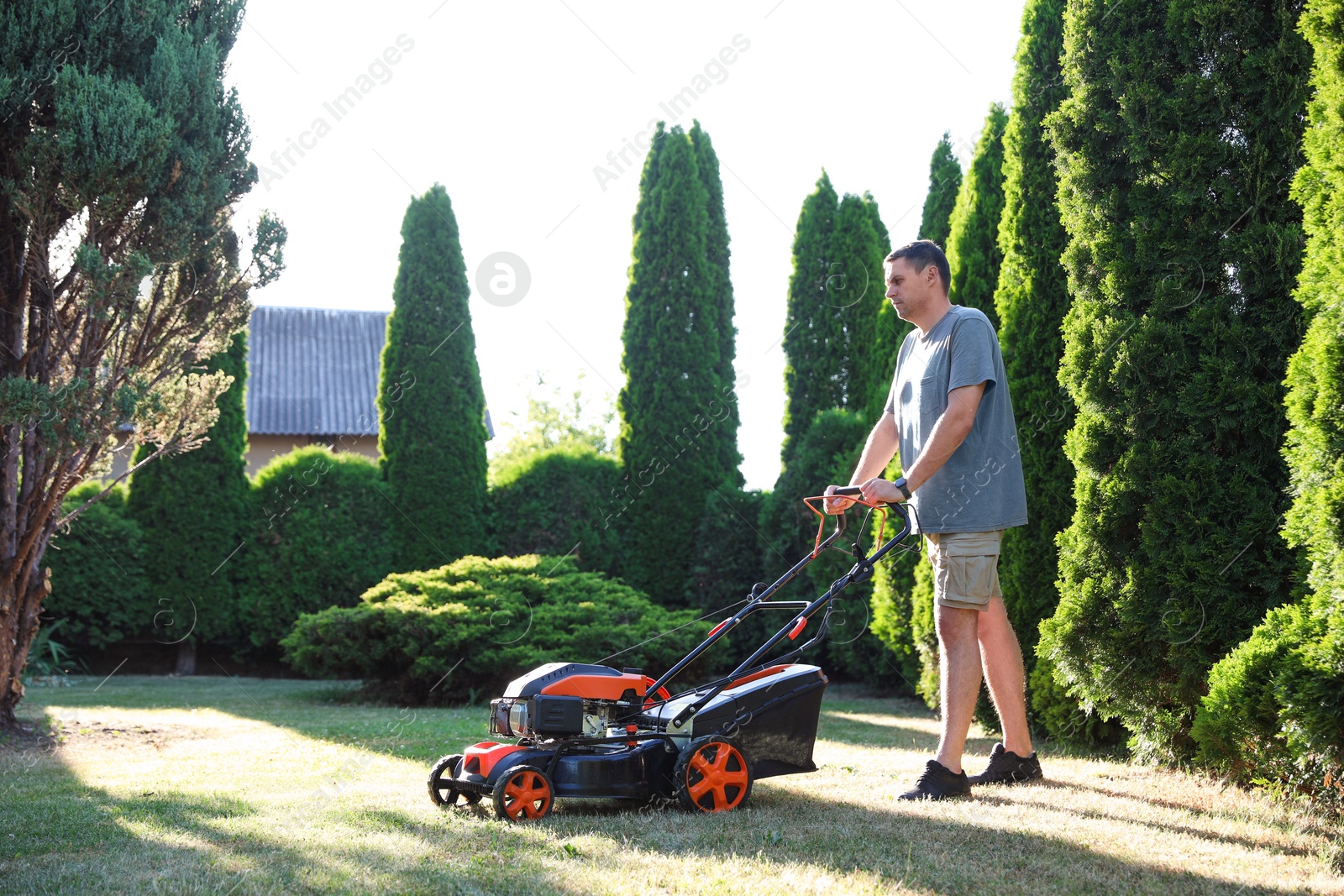 Photo of Man cutting green grass with lawn mower in garden