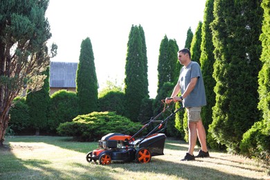 Photo of Man cutting green grass with lawn mower in garden