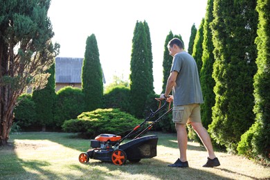 Photo of Man cutting green grass with lawn mower in garden