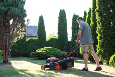 Photo of Man cutting green grass with lawn mower in garden