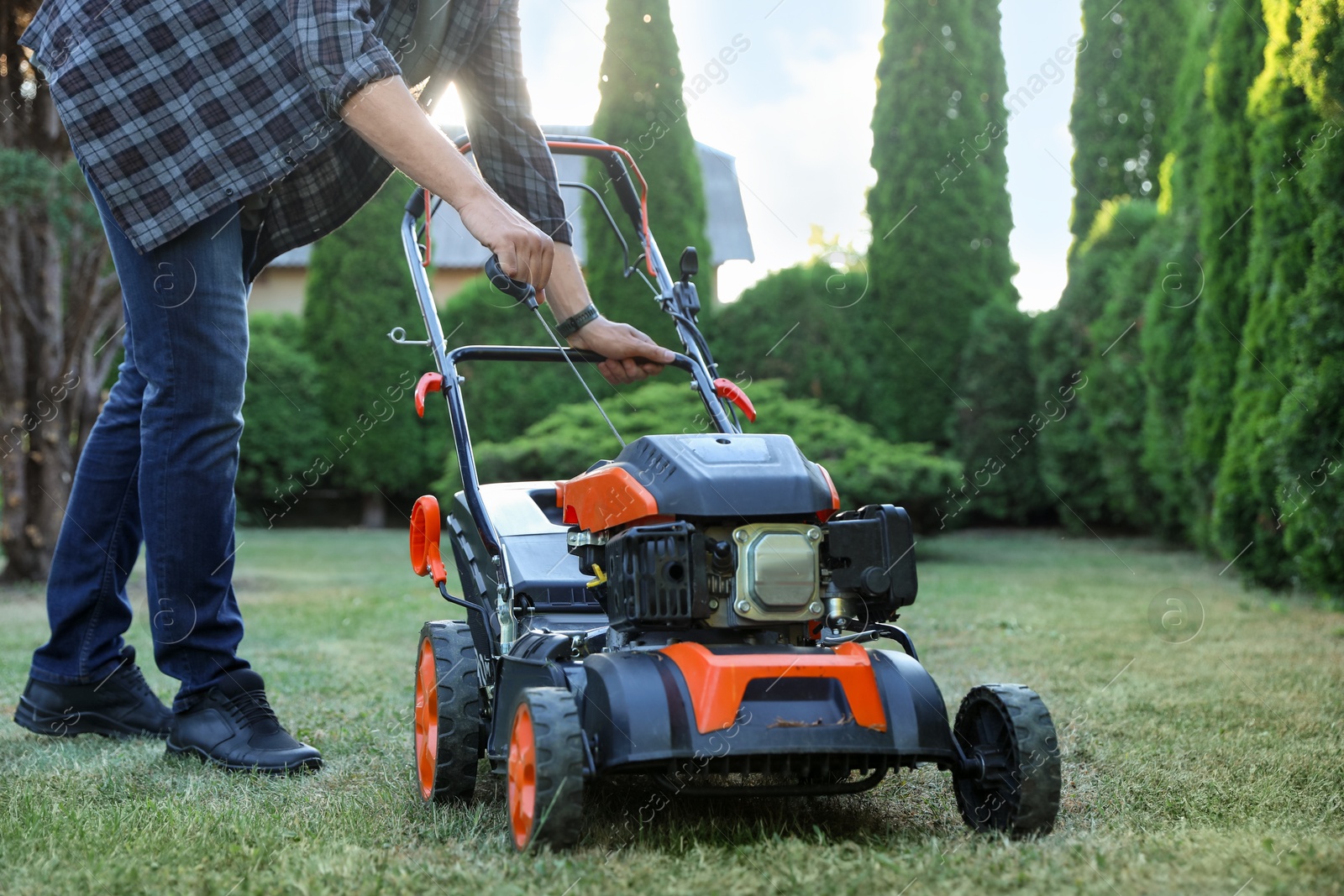 Man pulling starter cord of lawn mower in garden, closeup Photo of Man pulling starter cord of lawn mower in garden, closeup