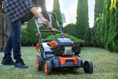 Photo of Man pulling starter cord of lawn mower in garden, closeup