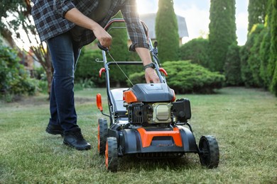 Photo of Man pulling starter cord of lawn mower in garden, closeup