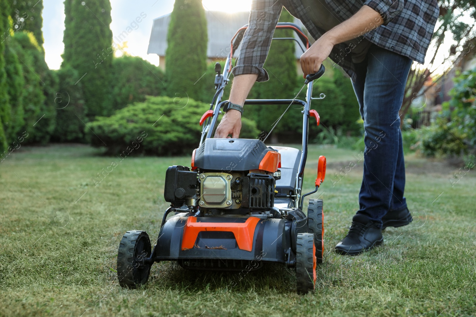 Photo of Man pulling starter cord of lawn mower in garden, closeup