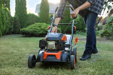Photo of Man pulling starter cord of lawn mower in garden, closeup