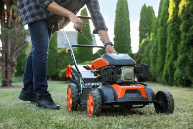 Photo of Man pulling starter cord of lawn mower in garden, closeup
