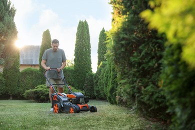 Photo of Man cutting green grass with lawn mower in garden