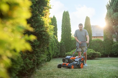 Photo of Man cutting green grass with lawn mower in garden