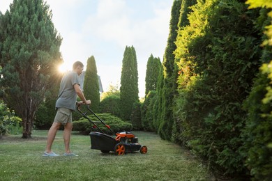 Photo of Man cutting green grass with lawn mower in garden