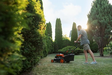 Photo of Man cutting green grass with lawn mower in garden