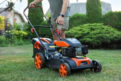 Photo of Man pulling starter cord of lawn mower in garden, closeup