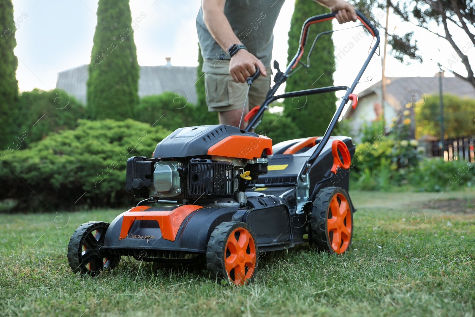 Photo of Man pulling starter cord of lawn mower in garden, closeup