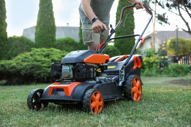 Photo of Man pulling starter cord of lawn mower in garden, closeup