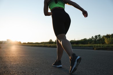 Photo of Woman in sportswear running on road outdoors, closeup. Space for text