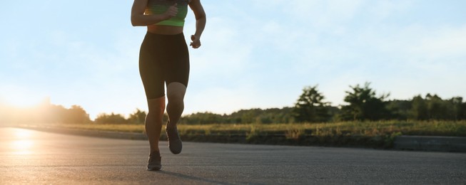 Photo of Woman in sportswear running on road outdoors, closeup. Space for text
