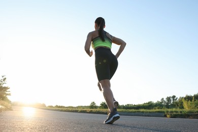 Photo of Woman in sportswear running on road outdoors, low angle view