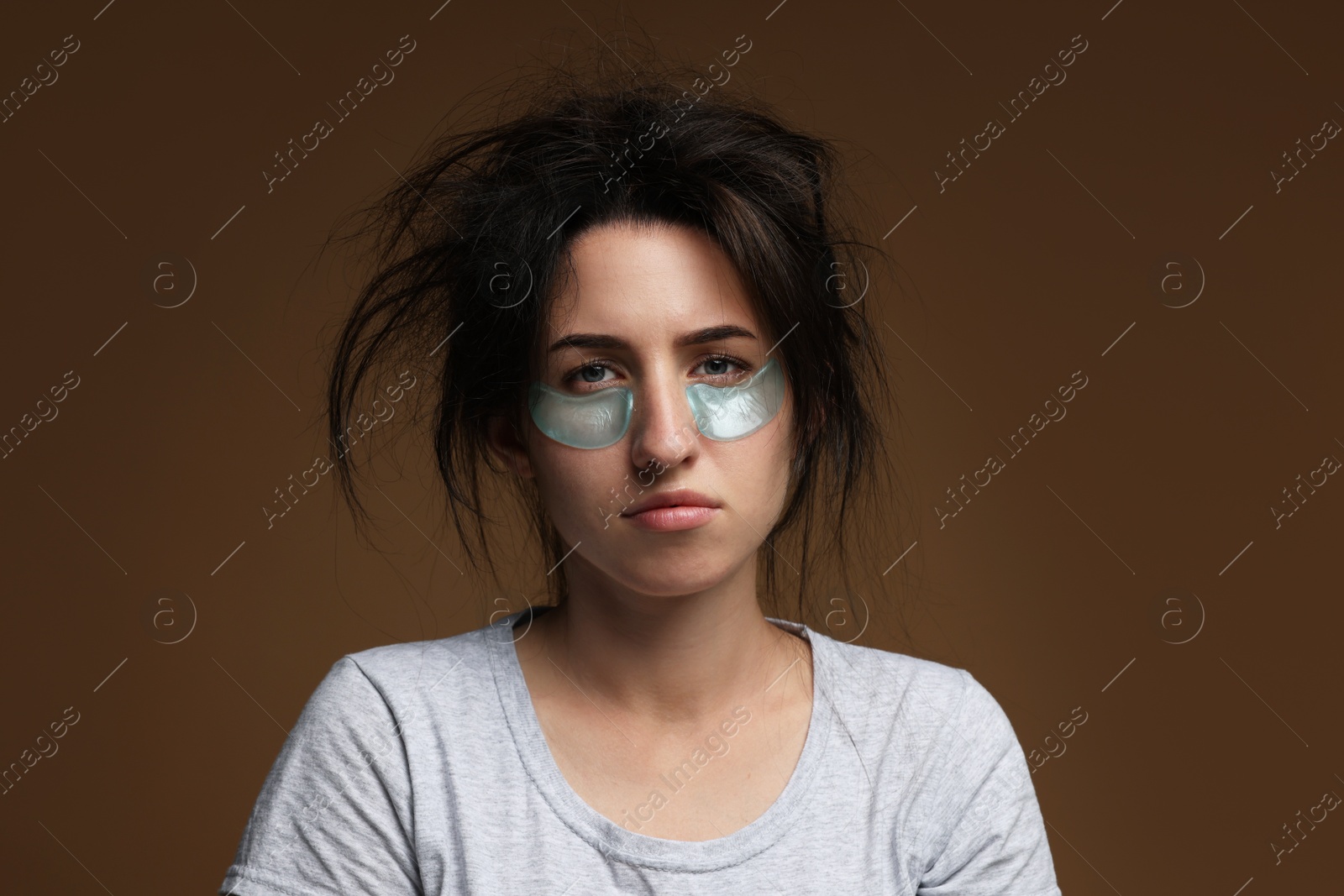 Photo of Woman with eye patches suffering from hangover on brown background