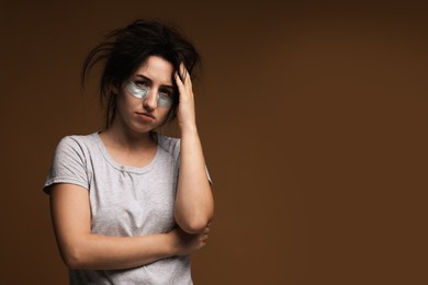 Photo of Woman with eye patches suffering from hangover on brown background, space for text