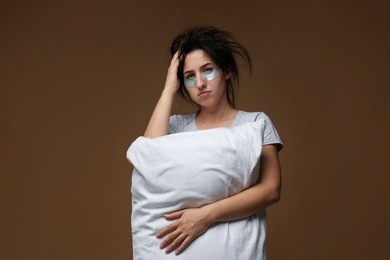 Photo of Woman with eye patches and pillow suffering from hangover on brown background